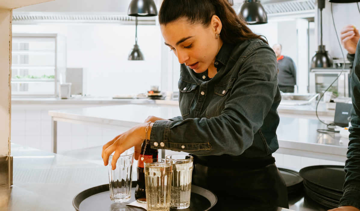 Serveur en restauration en tenue noire portant un plateau dans une salle de restaurant